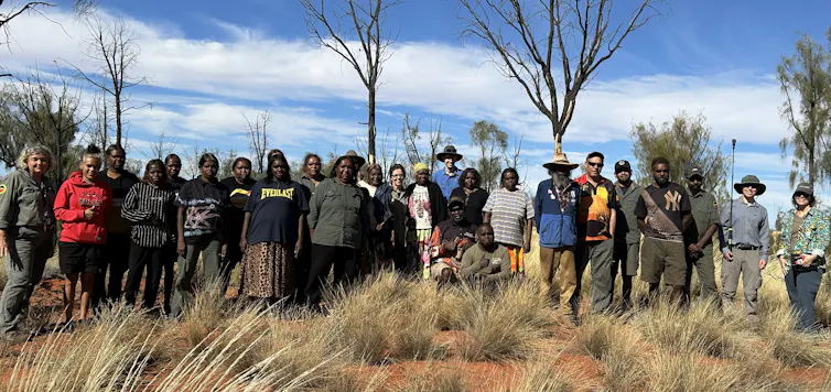 A large group of traditional owners and scientists standing together in a desert landscape.