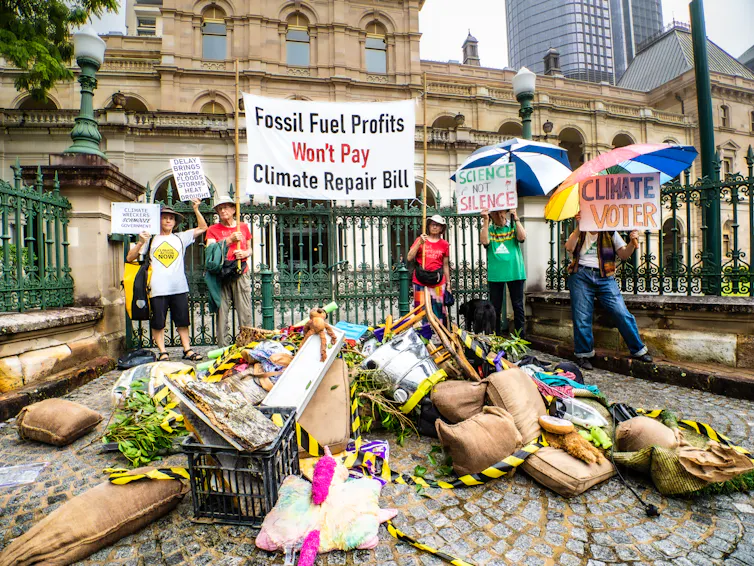 Several people hold signs critiquing the climate costs of fossil fuel projects.