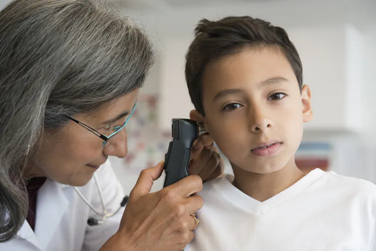 woman with glasses using otoscope to look into child's ear