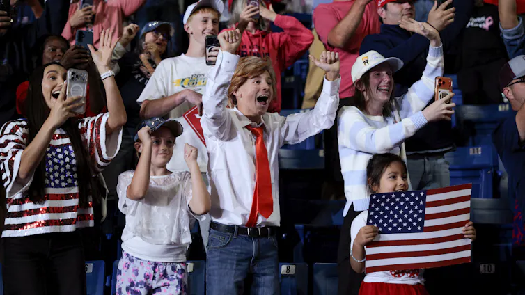 A group of people standing among bleachers, raising arms and cheering.