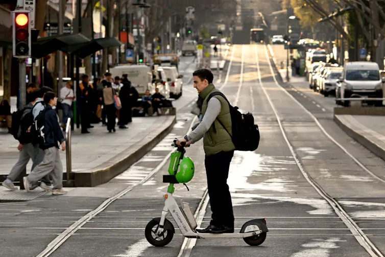 man riding e-scooter in city over tram tracks, no helmet.
