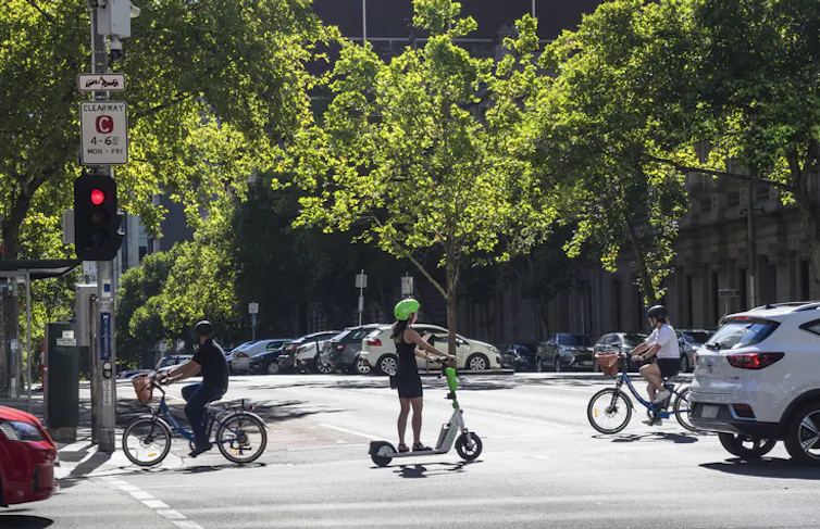 cityscape, trees background and people in cars, e-bikes and scooters.