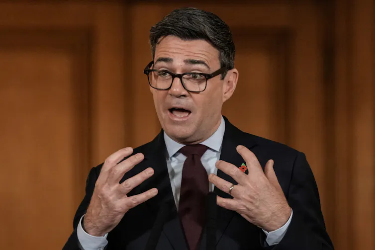 Bespectacled man speaking and gesticulating with both hands.