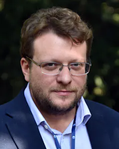 Headshot of a man with rimless spectacles and a short beard.