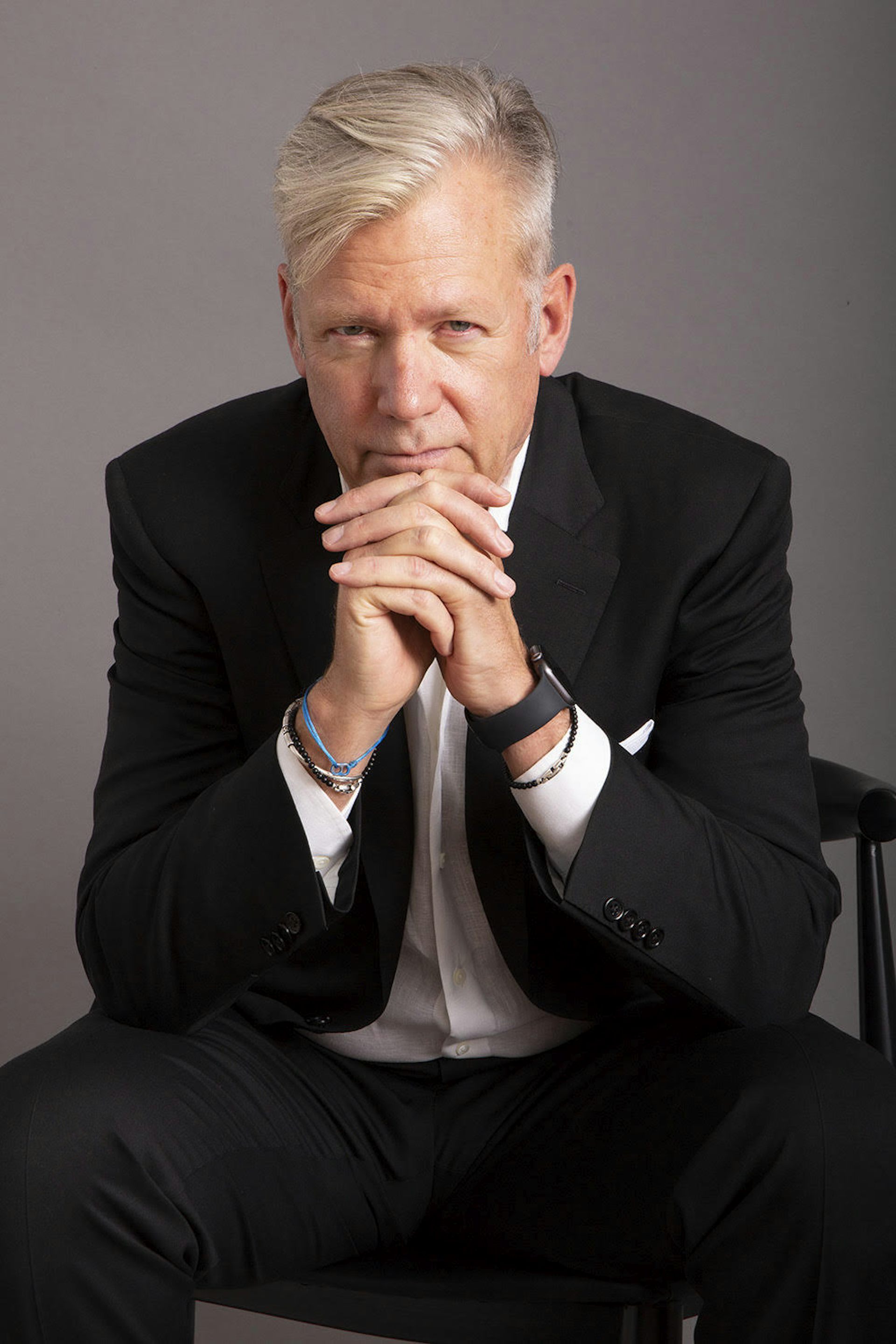 A middle-aged man sitting with his hands clasped under his chin.