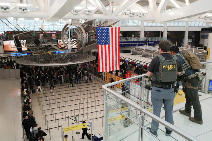 Two men wearing bulletproof vests overlook a line of passengers in an airport.