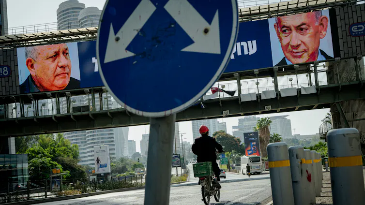 A road sign is seen with a billboard with two men in the background.