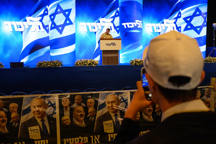 A man in a white hat takes a picture of someone on a stage.
