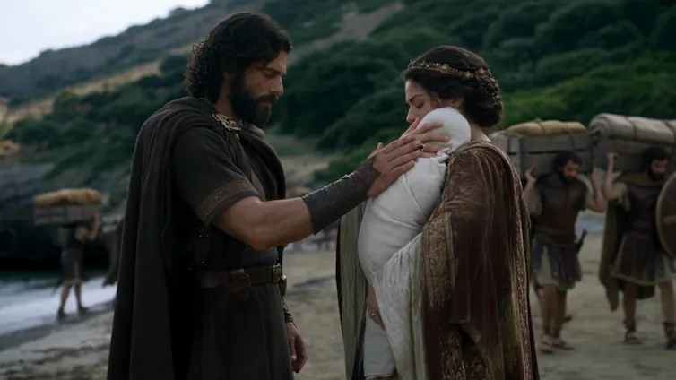 Screenshot of film: a man says goodbye to his wife and baby on a beach.