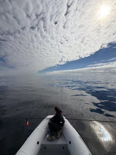 A man sits in a boat on the ocean on a fairly cloudy day.