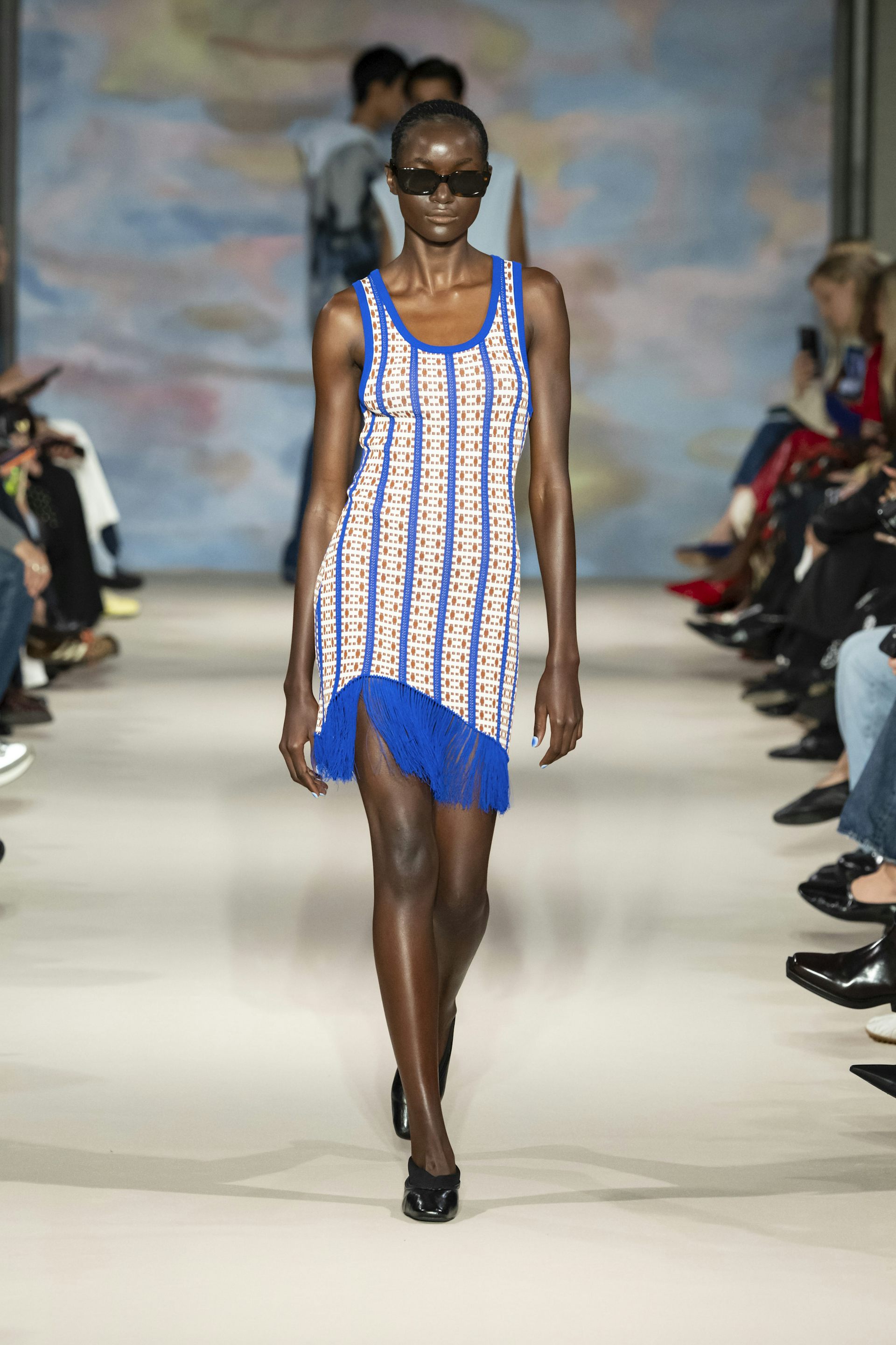 A woman walking down a catwalk in bright blue and cream patterned dress.