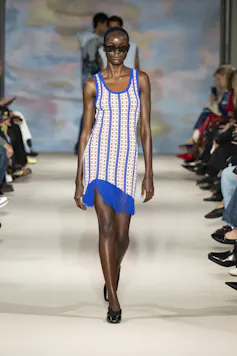 A woman walking down a catwalk in bright blue and cream patterned dress.